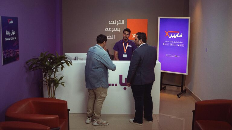 Three men conversing at a help desk in a modern office setting.